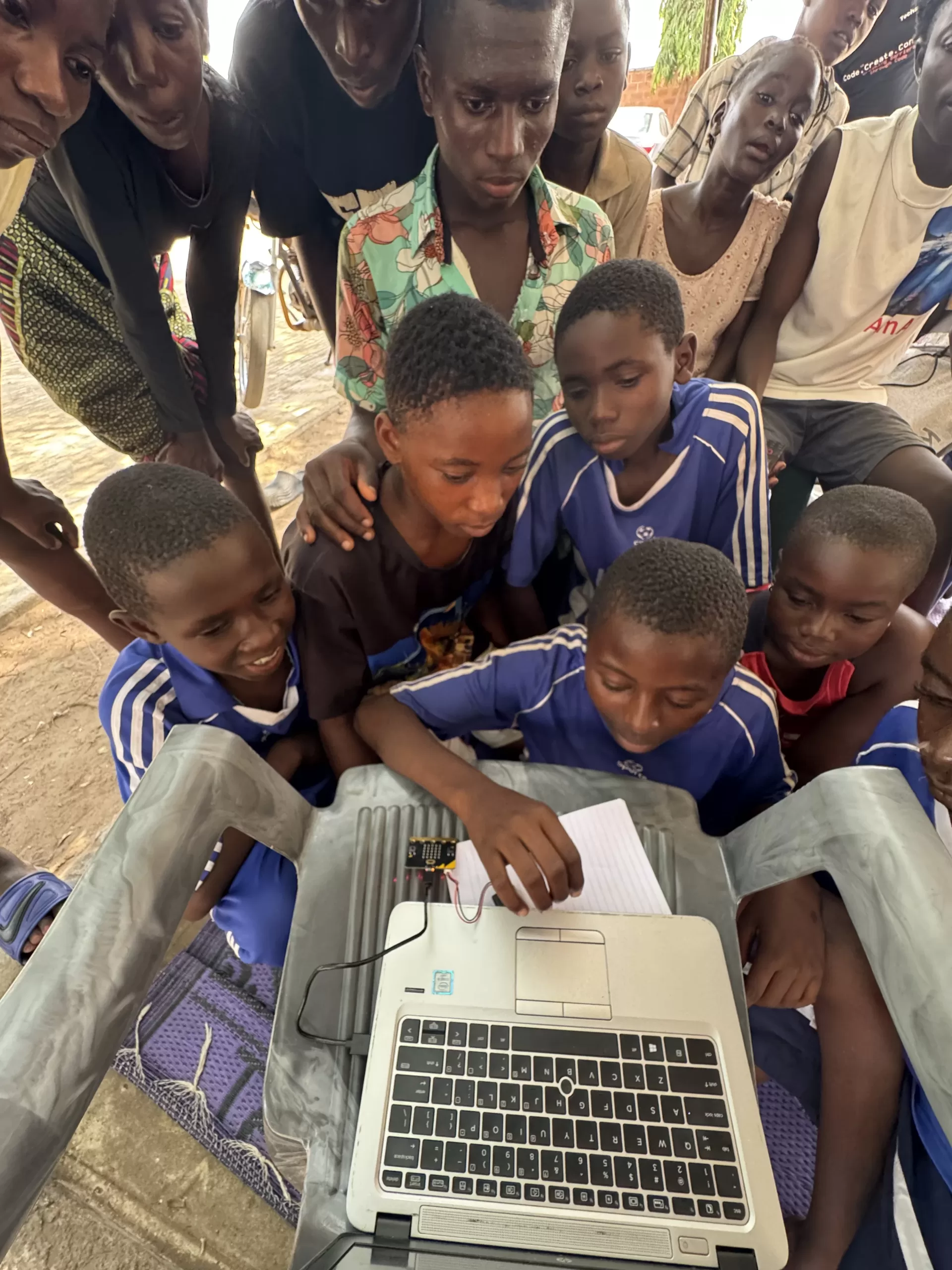 Diverse group of children in rural community setting working together on robotics project, outdoor learning environment
