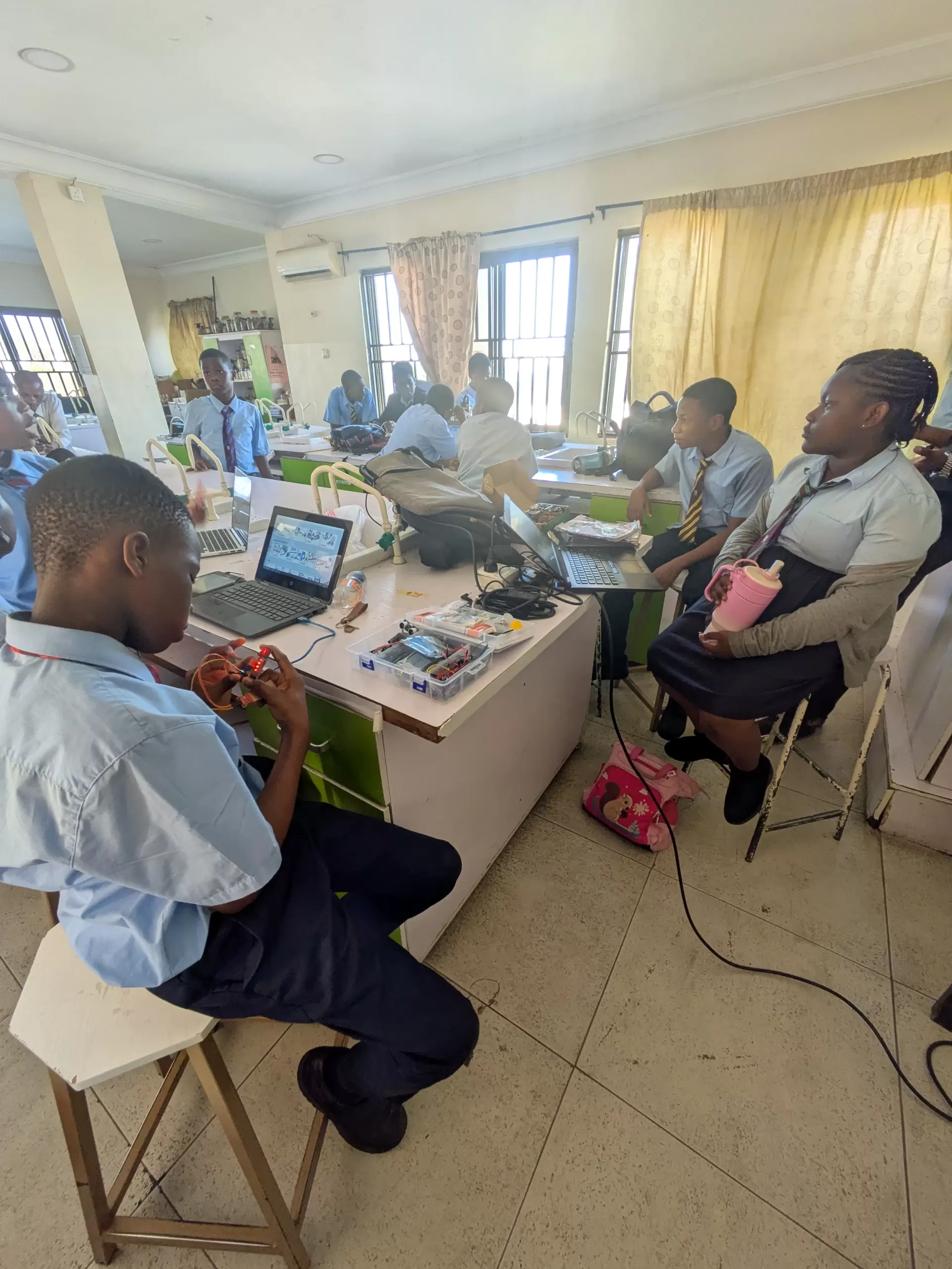 Smiling female teacher guiding diverse group of middle school students working with robotics kits in bright modern classroom